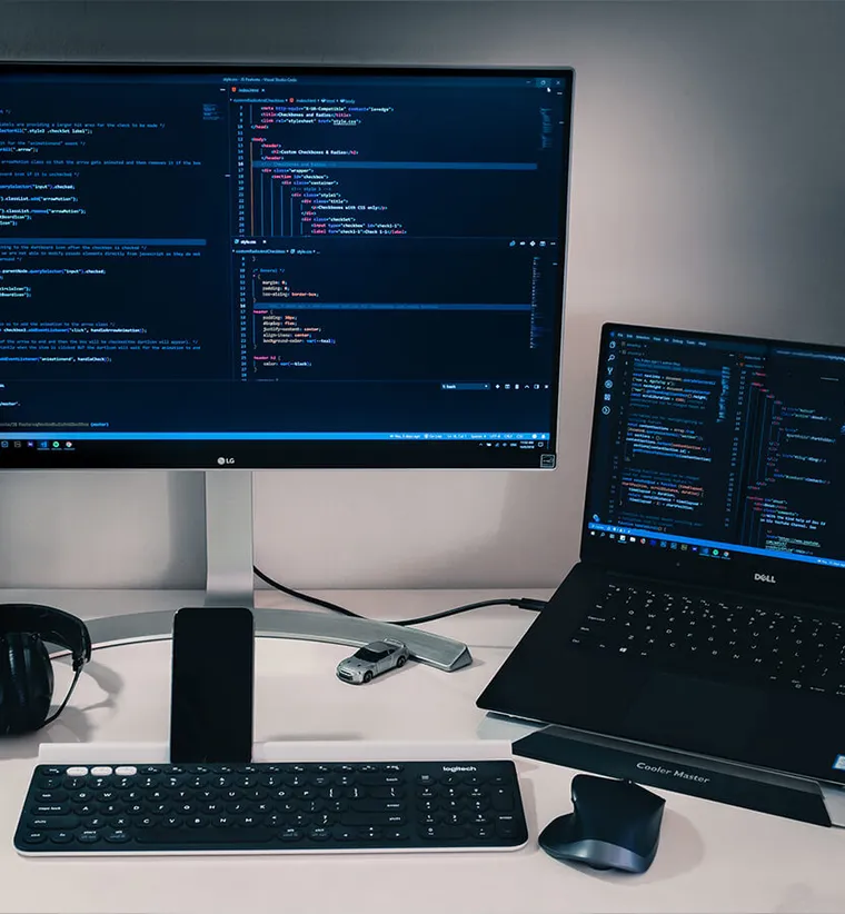 Desk with a monitor and laptop showing code