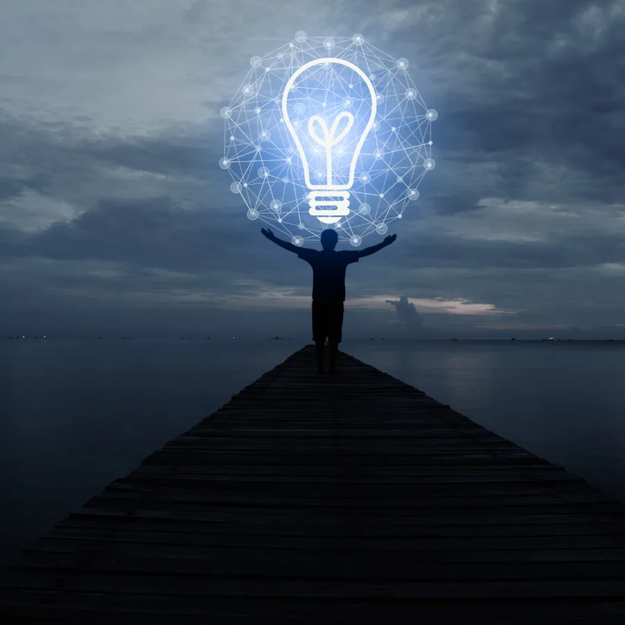 Person on a jetty at dusk beneath a glowing lightbulb