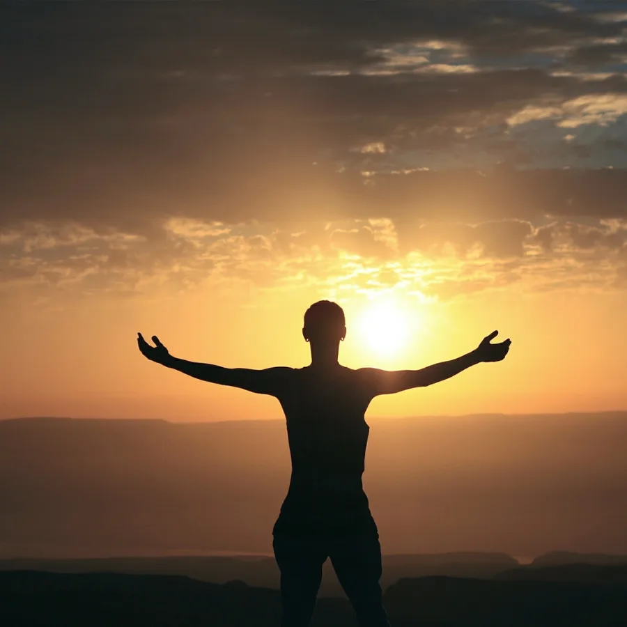 Person standing arms outstretched against a sunset