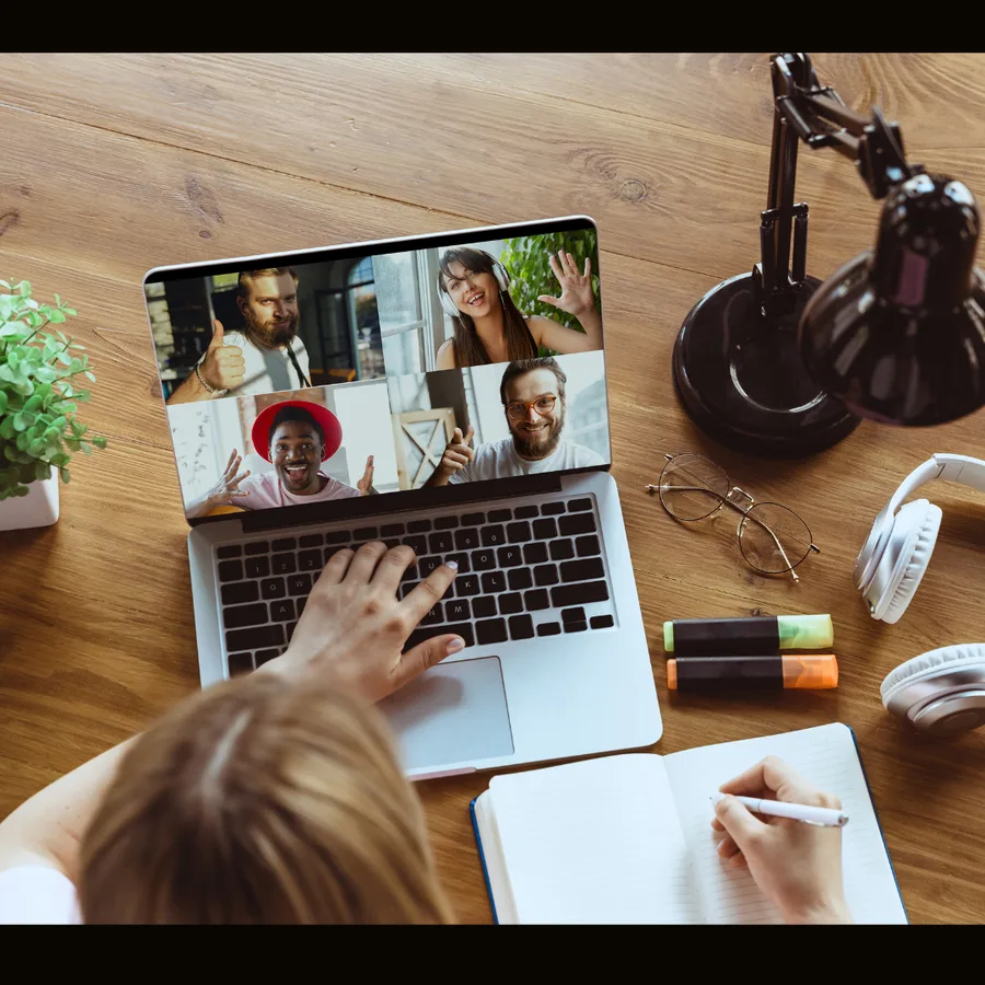 Video call on a laptop at a home desk with a notebook alongside