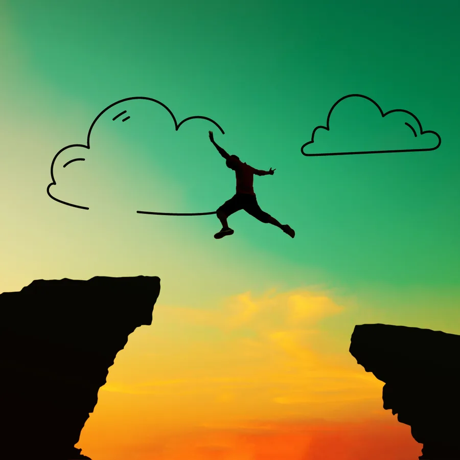 Silhouette of a person leaping between two clifftops at sunset