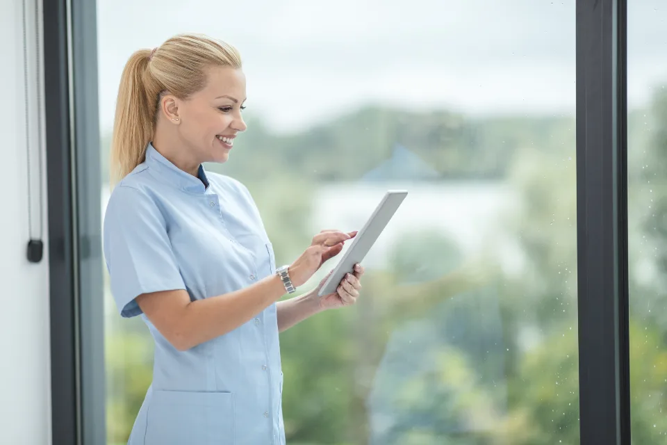 Carer recording notes on a tablet by a window