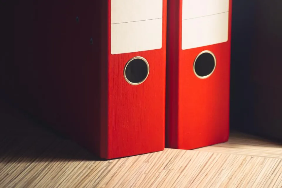 Two red lever-arch files standing on a wooden floor