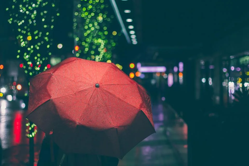 Person sheltering under a red umbrella on a rainy city street at night