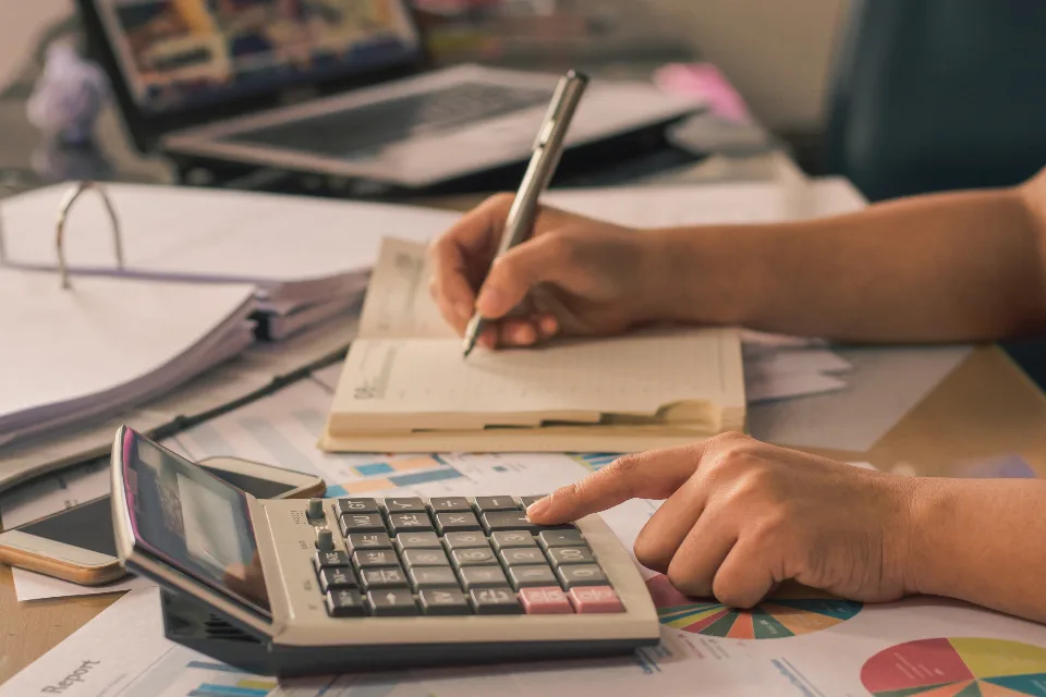Working through figures on a calculator beside a notebook and charts
