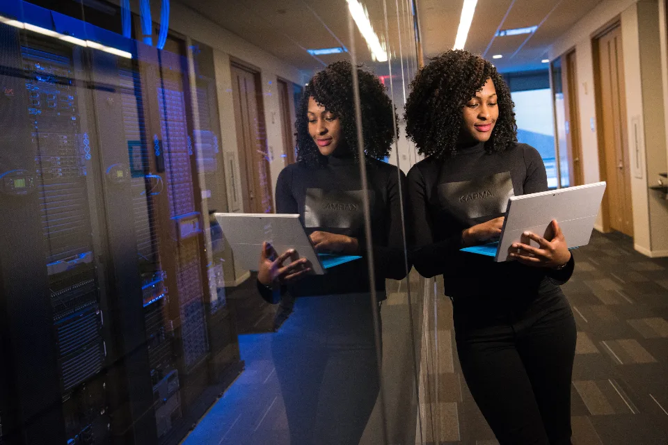 Engineer with a laptop beside a glass-walled server room
