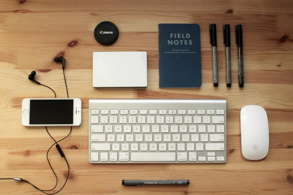 Phone, keyboard, hard drive and notebook laid out on a desk